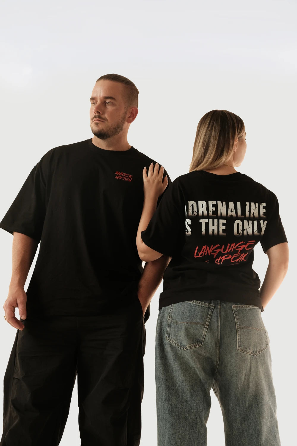 Male and female models wearing Racer Nation Adrenaline Only black oversized tee showing front chest print and large back graphic