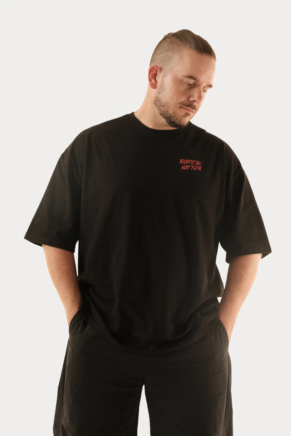 Male model wearing Racer Nation Adrenaline Only black oversized tee showing red front chest logo and relaxed fit
