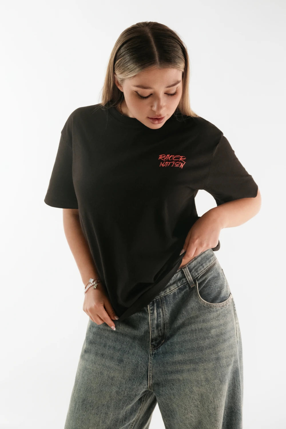 Female model wearing Racer Nation Adrenaline Only black oversized tee showing red front chest logo and relaxed oversized fit