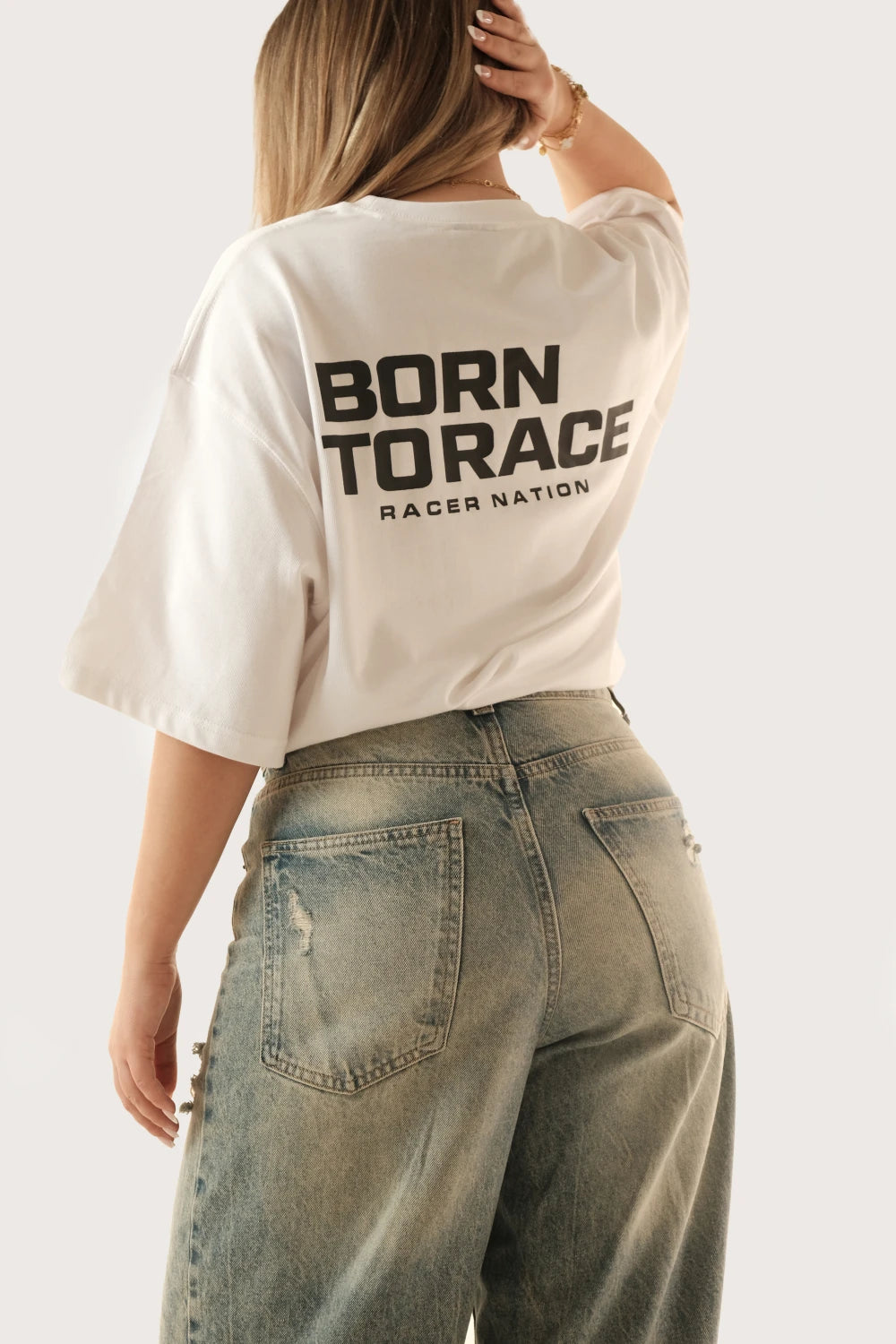 Female model wearing Racer Nation Born To Race white oversized tee showing the black back graphic and relaxed fit
