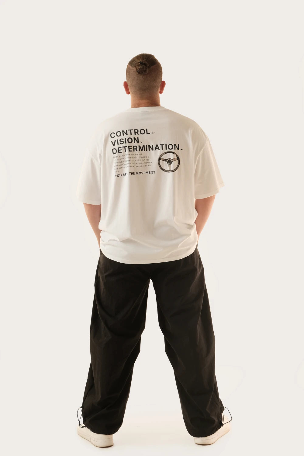 Male model wearing Racer Nation Full Focus white oversized tee showing Control Vision Determination back print and steering wheel graphic
