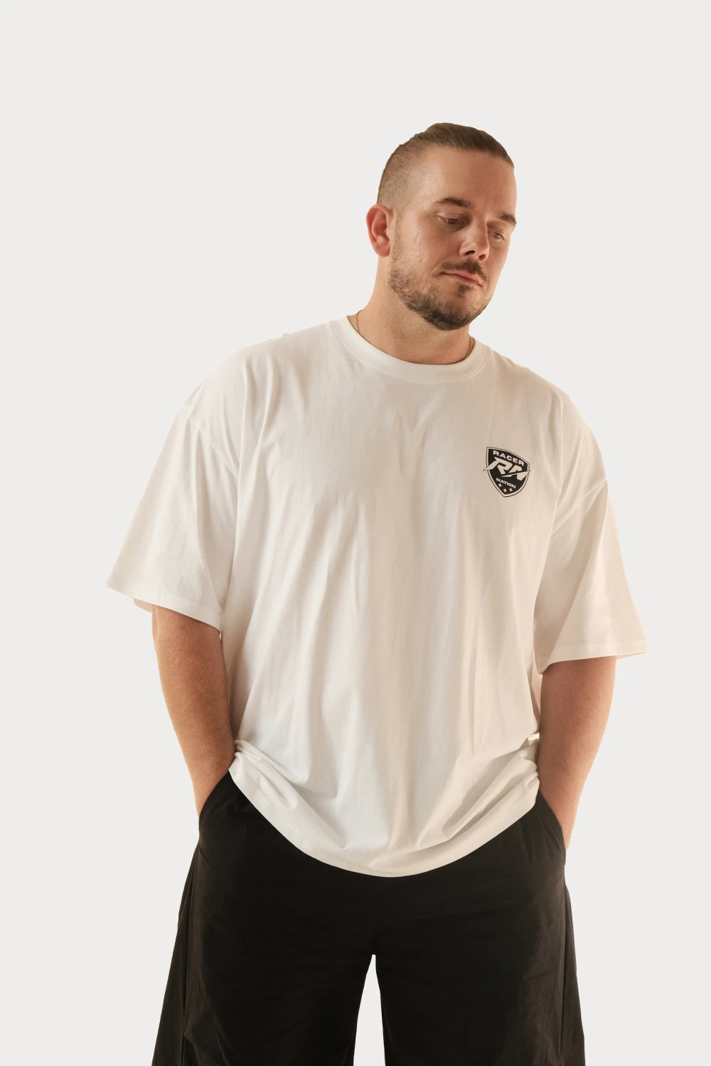 Male model wearing Racer Nation Full Focus white oversized tee showing black front chest graphic and relaxed oversized fit