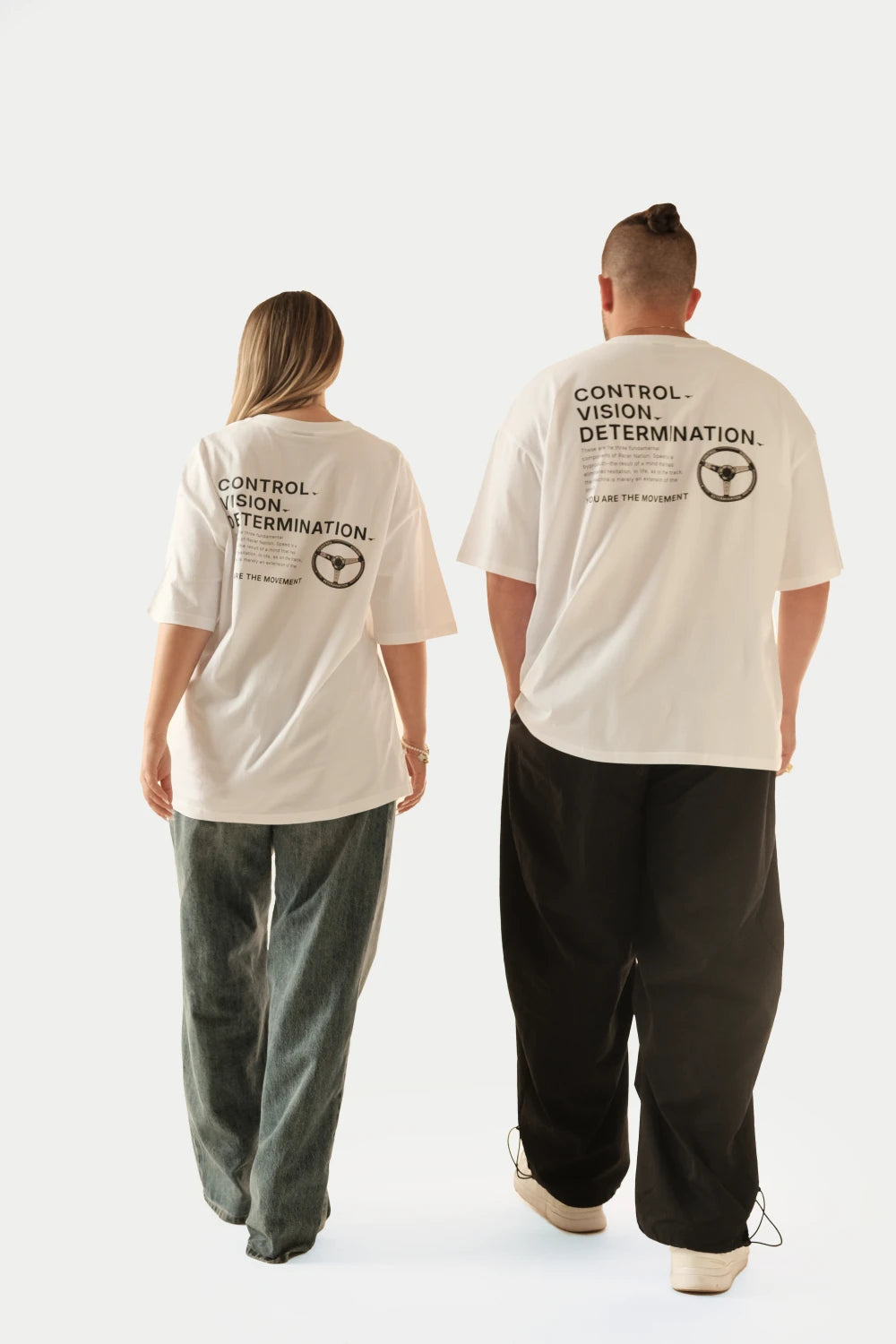 Male and female models wearing Racer Nation Full Focus white oversized tees showing Control Vision Determination back print and steering wheel graphic