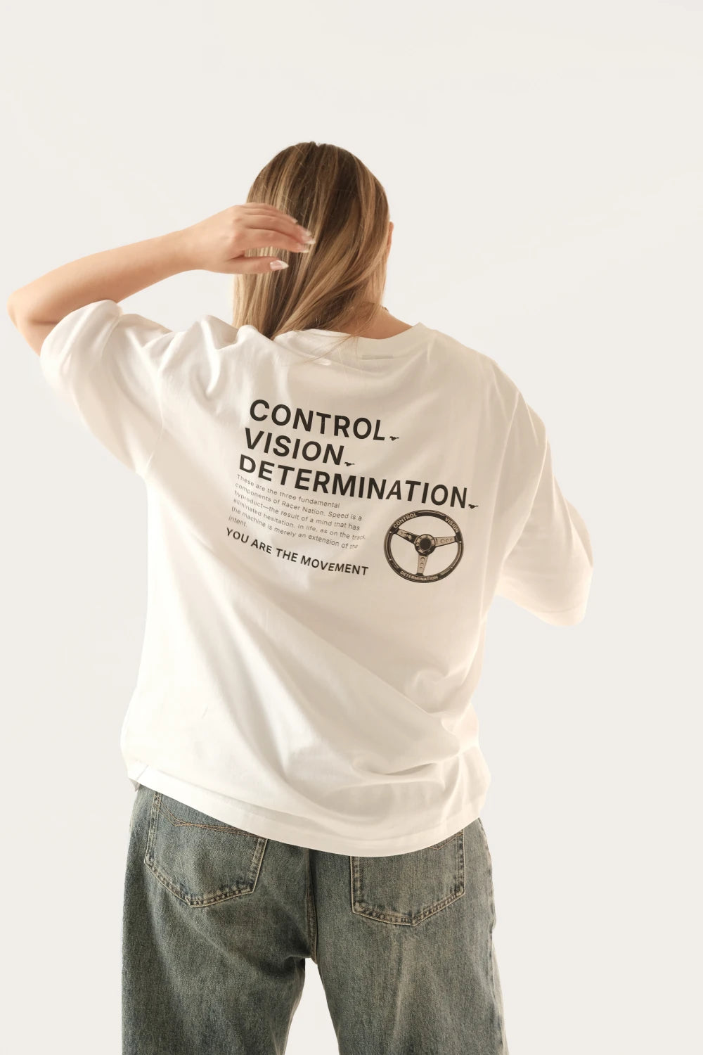 Female model wearing Racer Nation Full Focus white oversized tee showing Control Vision Determination back print and steering wheel graphic