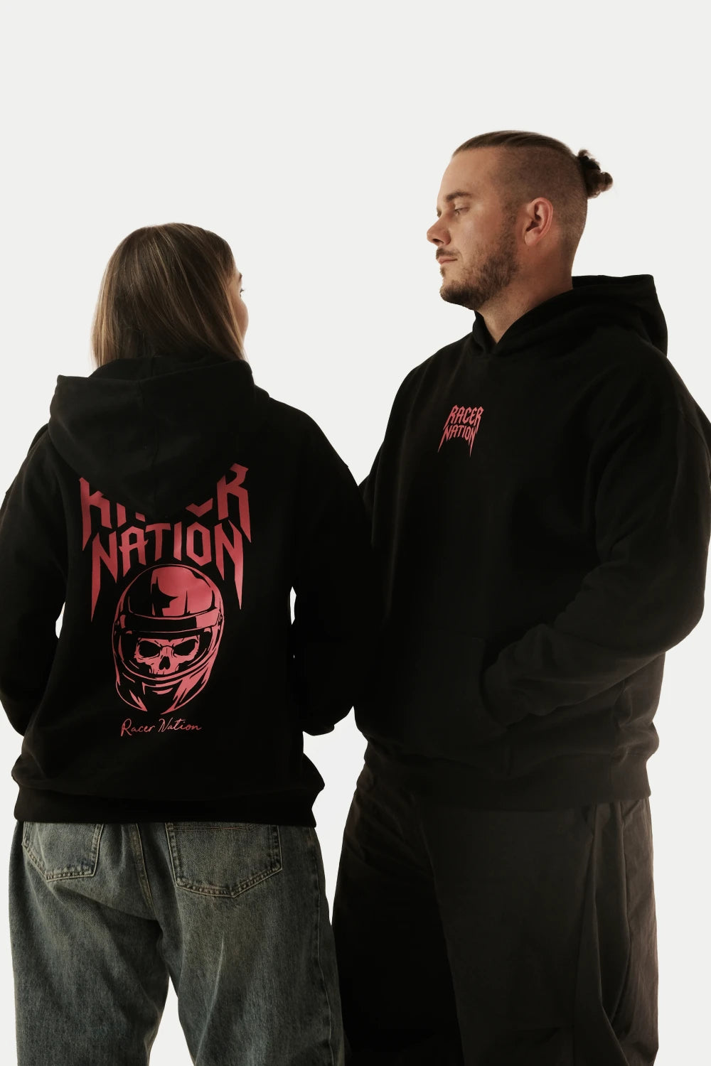 Male and female models wearing the Racer Nation Ghost Rider black oversized hoodie, showing the front logo and skull helmet back graphic.