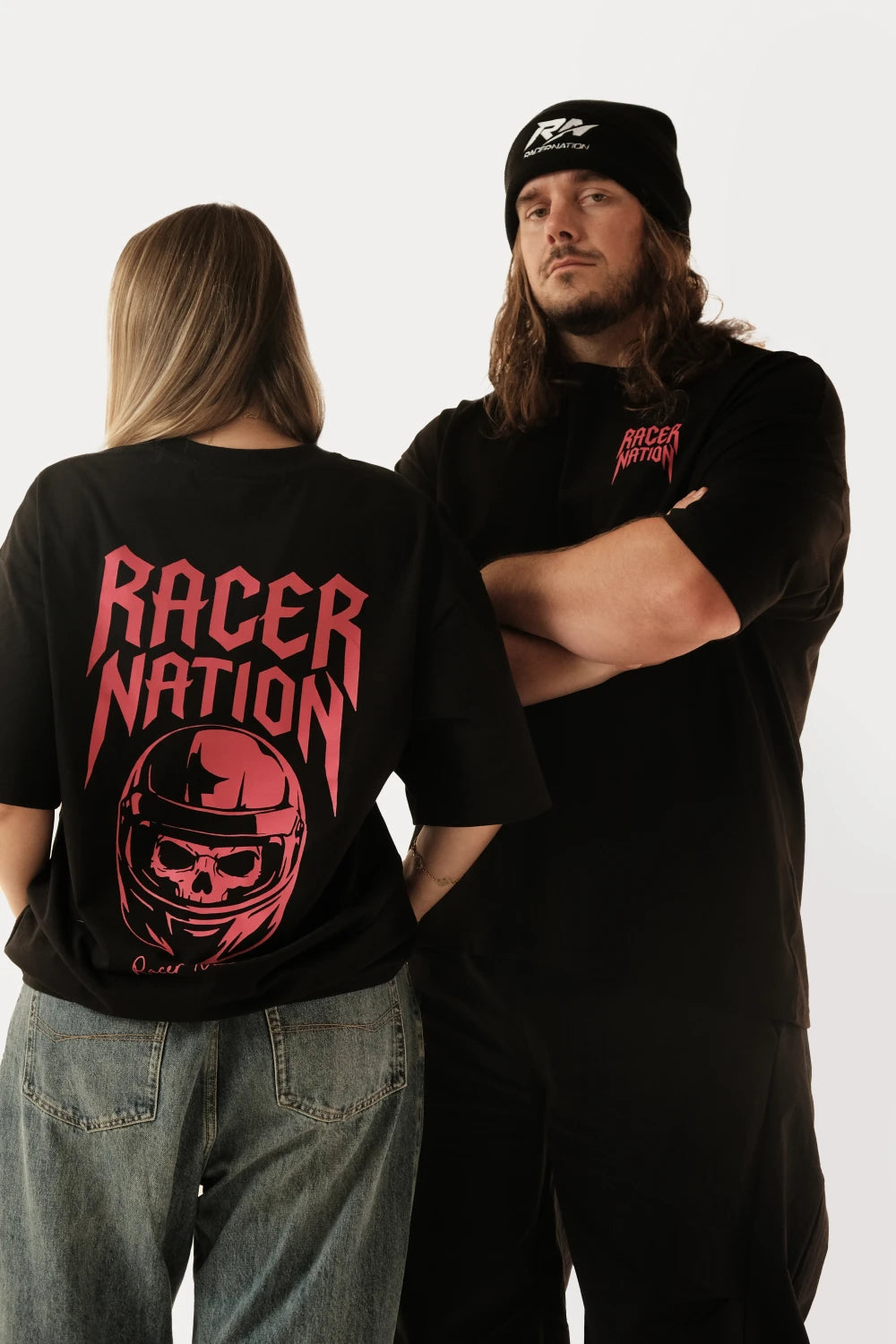 Male and female models wearing Racer Nation Ghost Rider black oversized tee showing front chest print and red helmet back graphic