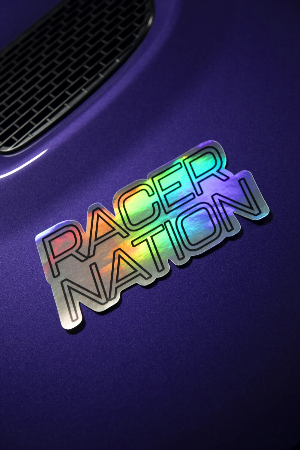 Holographic Racer Nation logo sticker displayed on a purple car, showing its colour-shifting reflective finish.