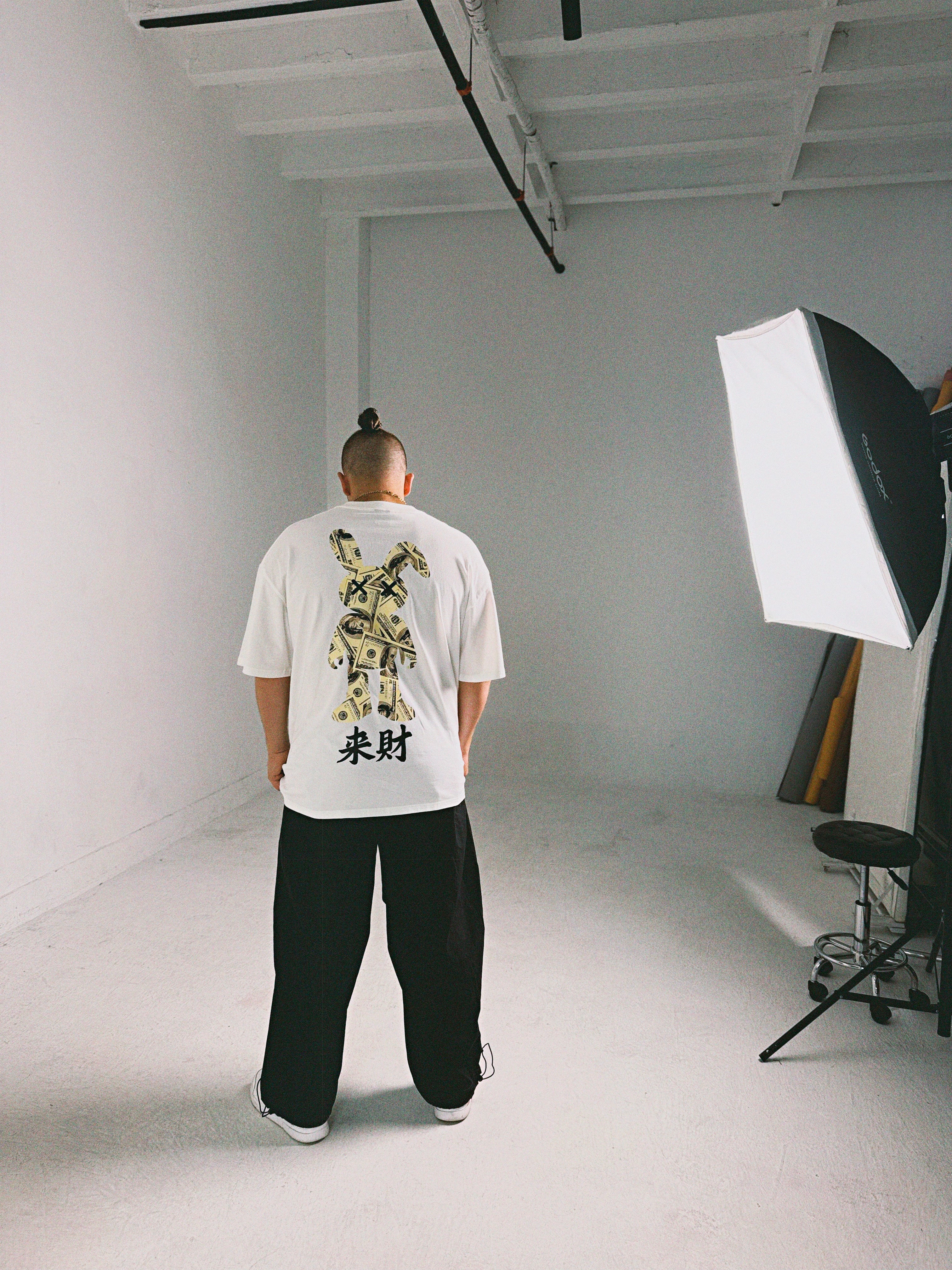 Male model wearing Racer Nation Money Bunny white oversized tee showing large black and gold bunny back graphic