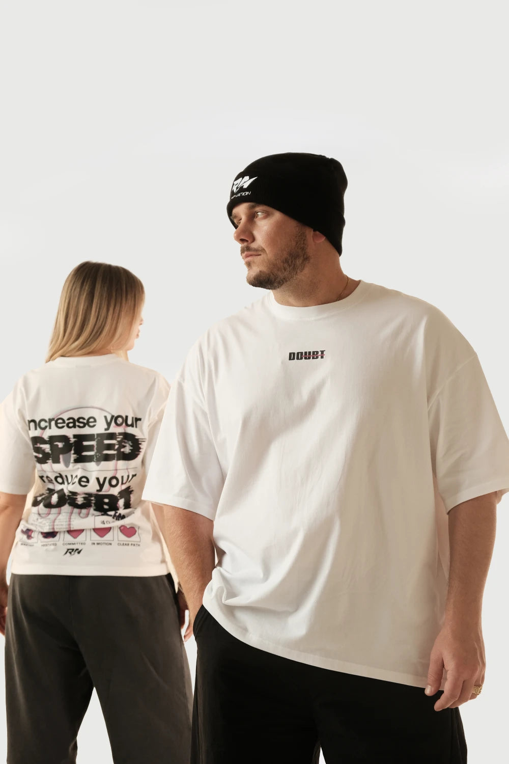 Male and female models wearing Racer Nation No Doubt white oversized tee showing front chest logo and Increase Your Speed Reduce Your Doubt back graphic