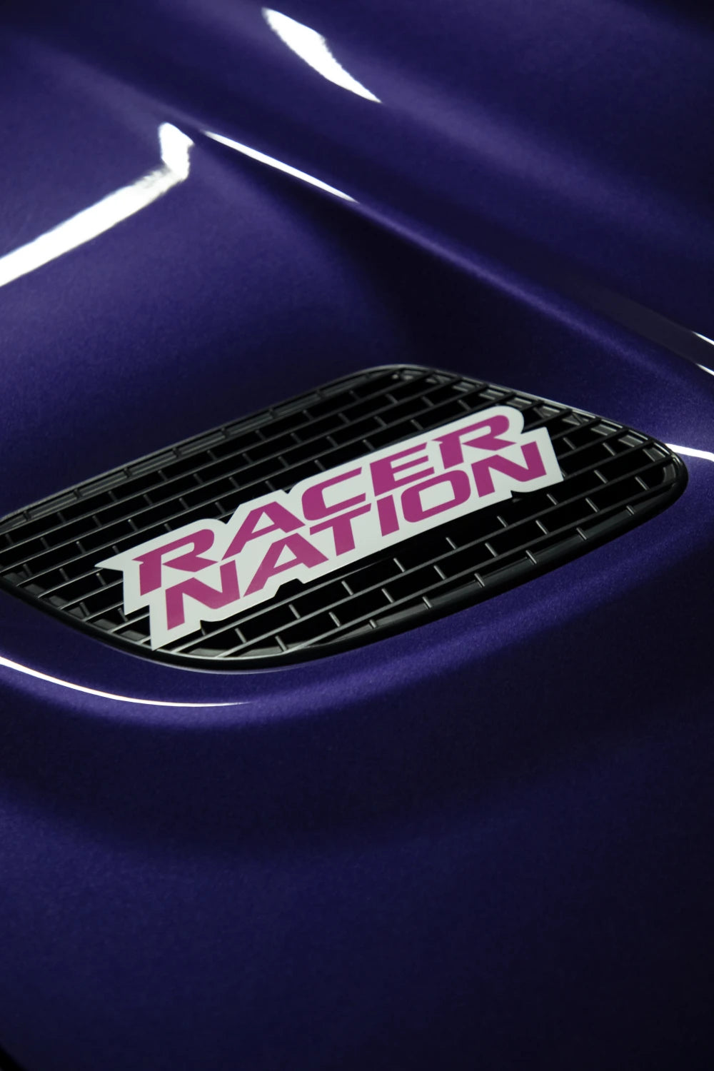 Pink and white Racer Nation logo sticker displayed on the grille of a purple car.