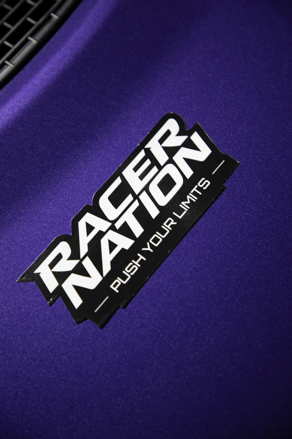 Black and white Racer Nation Push Your Limits die cut sticker displayed on a purple car.