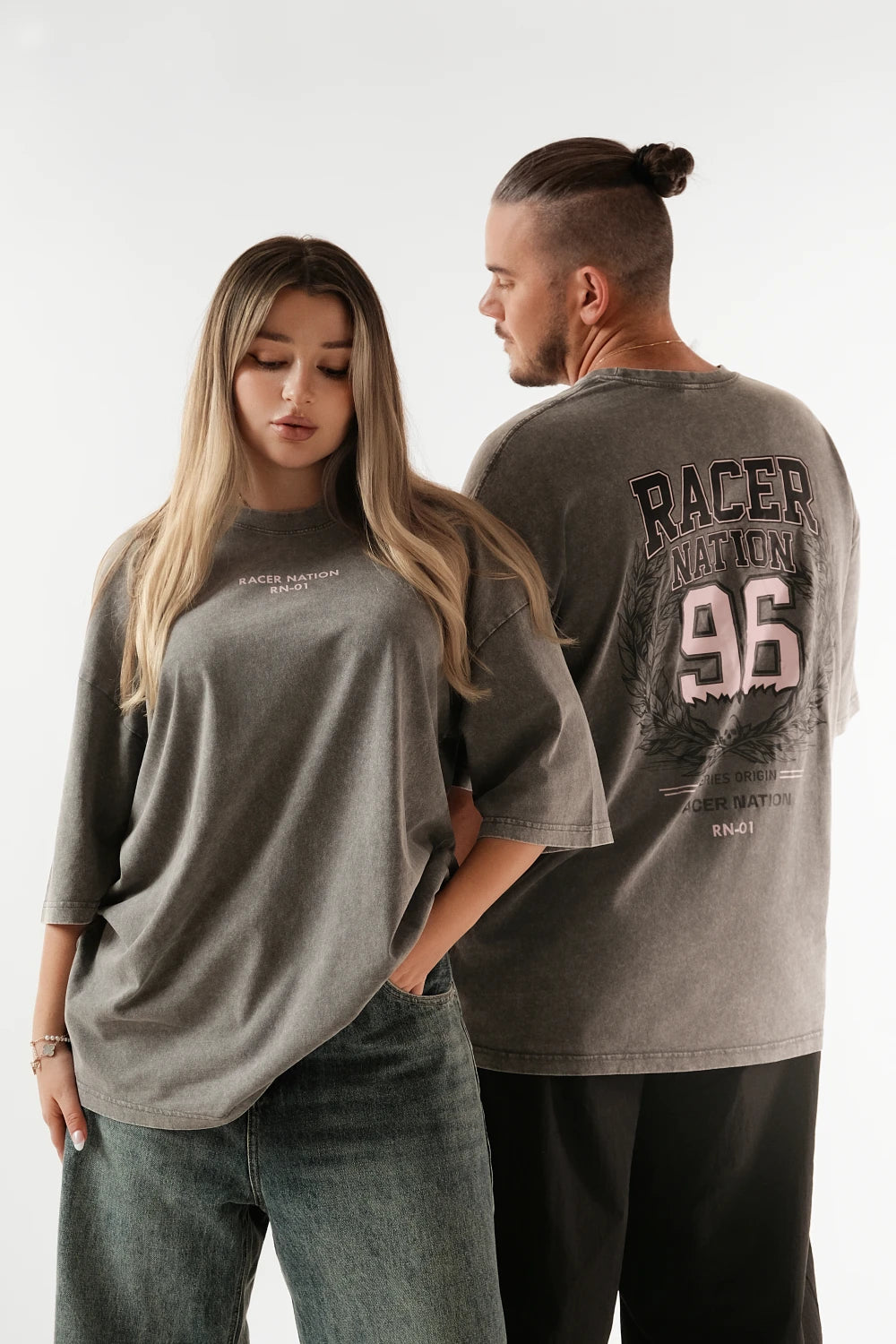 Male and female models wearing Racer Nation RN 01 grey acid washed oversized tee showing small front logo and large 96 back graphic