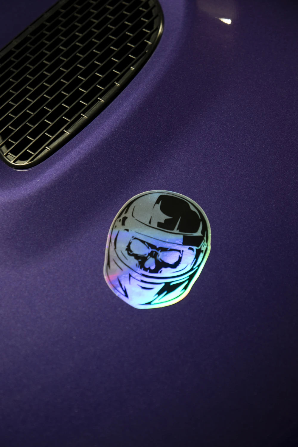 Holographic Racer Nation skull helmet sticker displayed on the bonnet of a purple car, showing its reflective finish.