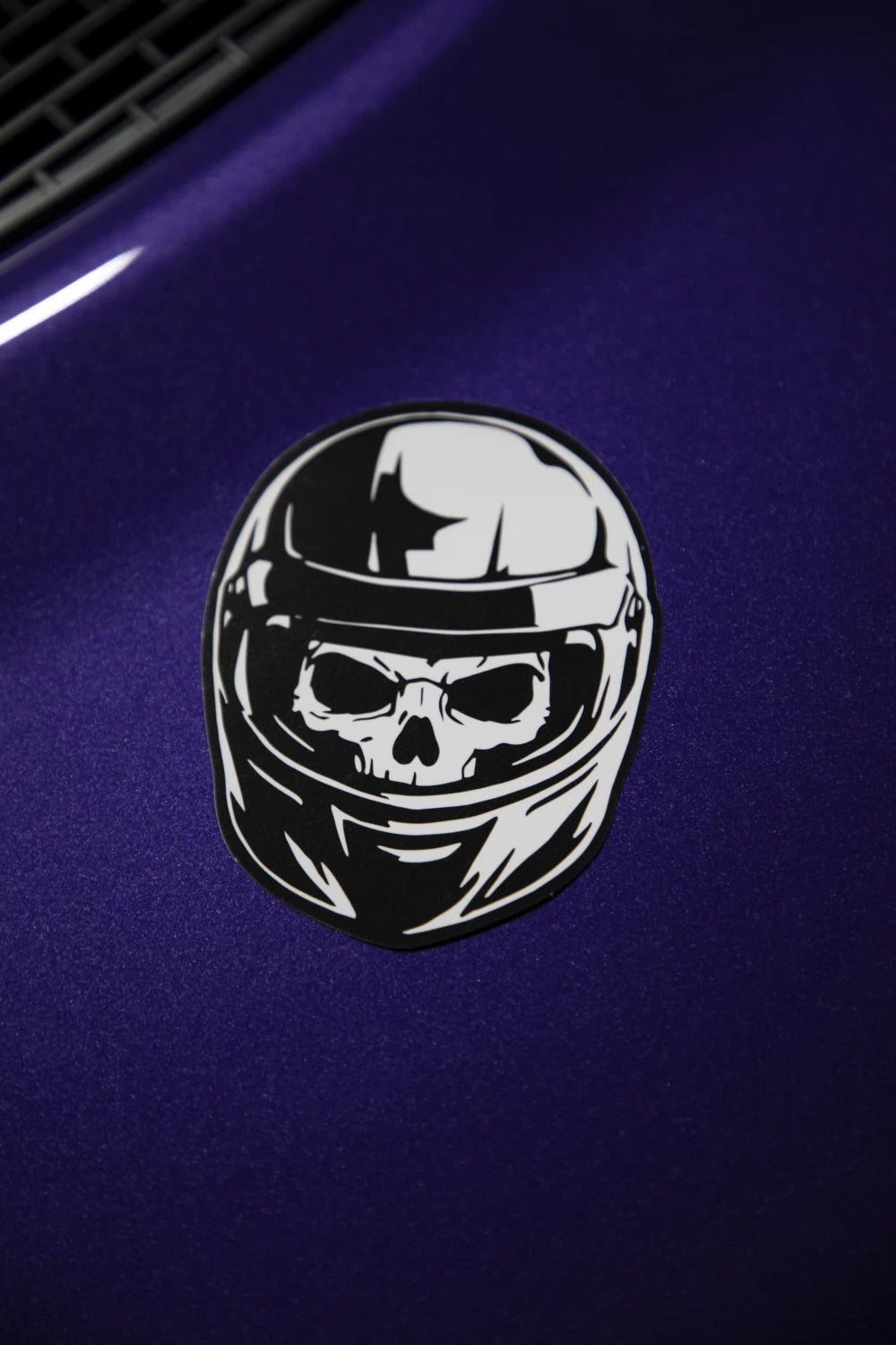 Black and white Racer Nation skull helmet sticker displayed on the bonnet of a purple car.