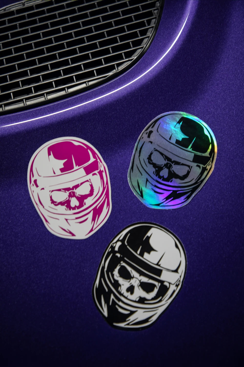 Racer Nation skull helmet stickers in pink and white, holographic, and black and white displayed on a purple car.
