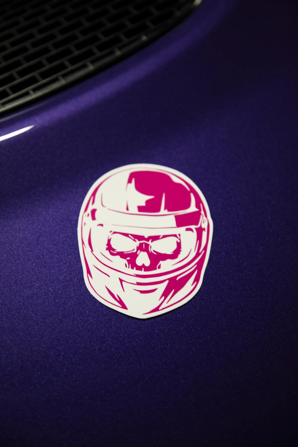 Pink and white Racer Nation skull helmet sticker displayed on the bonnet of a purple car.