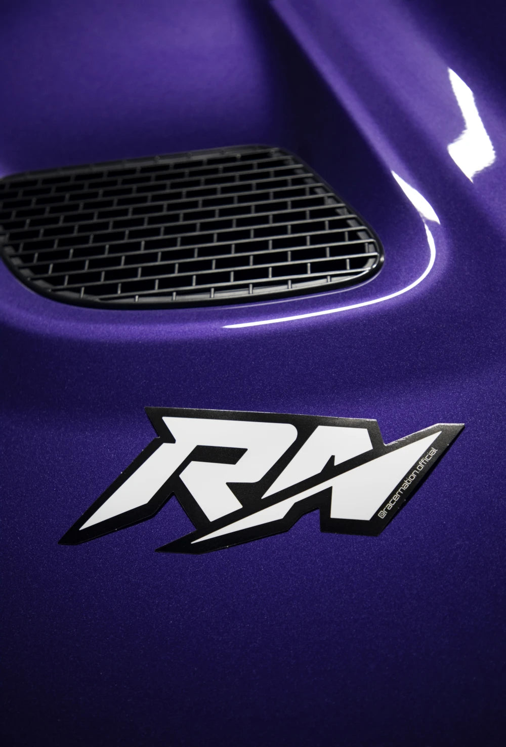Small black and white Racer Nation RN logo sticker displayed on the bonnet of a purple car.