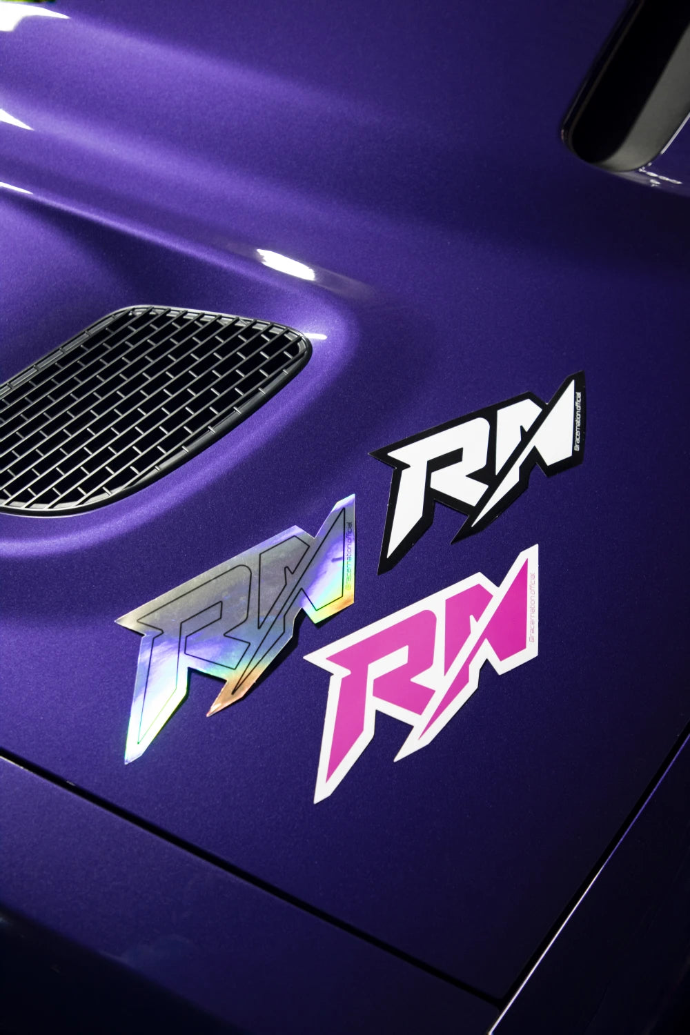 Small Racer Nation RN logo stickers in holographic, black and white, and hot pink displayed on a purple car.